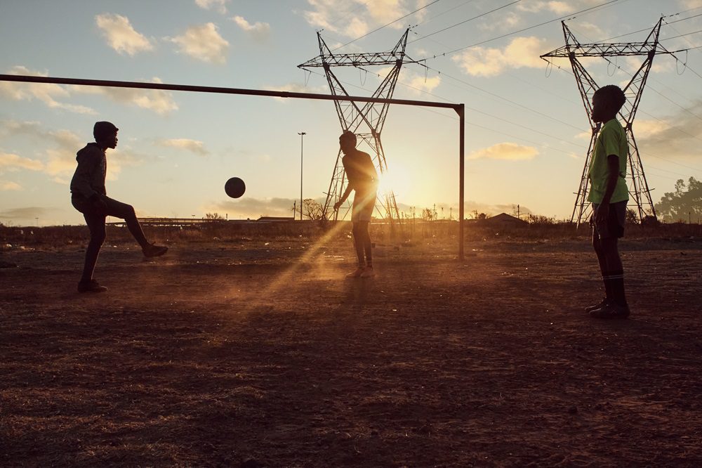 young african boys playing soccer football in an informal settlement township on dirt field